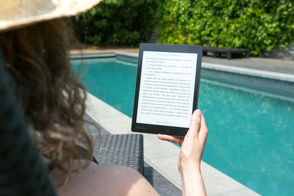 A woman relaxes by the pool, reading an e-reader for leisure. Perfect summer relaxation.